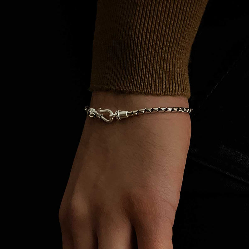 Een model in een bruine trui showt de minimalistische heren armband van sterlingzilver van Emir, verkrijgbaar via Ninetwofive.