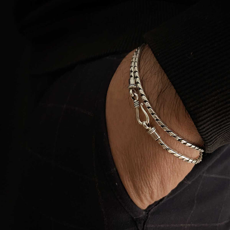 De pols van een man met de minimalistische heren armband ‘Emir’ van sterlingzilver, handen in de zak van een zwarte broek, Ninetwofive.