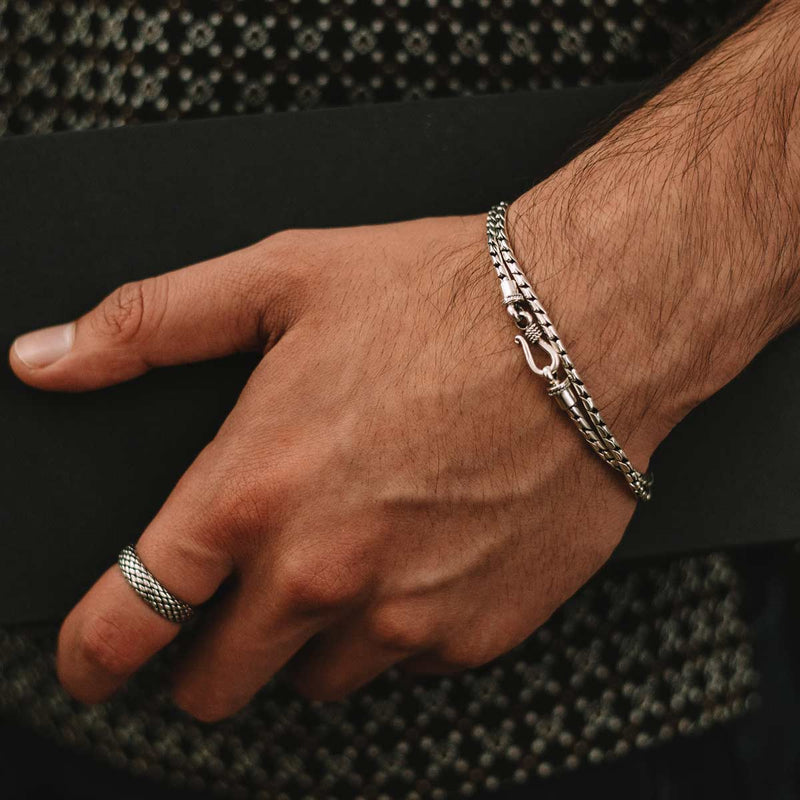 Een man die de minimalistische armband ‘Emir’ van Ninetwofive in sterlingzilver vasthoudt, samen met een zwarte box, terwijl hij een geoxideerde ring draagt.