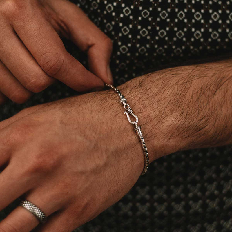Een man die in één hand de minimalistische heren armband ‘Emir’ van sterlingzilver vasthoudt en een geoxideerde ring draagt, Ninetwofive.