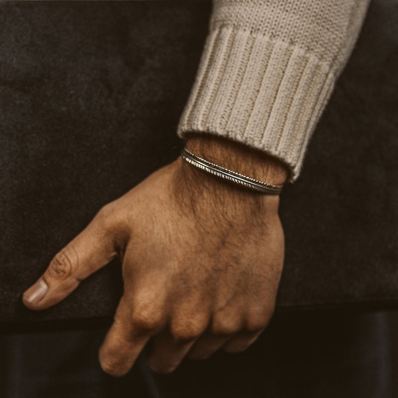 Gros plan sur la main d'un homme tenant délicatement le bracelet pour homme « Zahir » en argent, orné d'une plume, de la marque Ninetwofive.