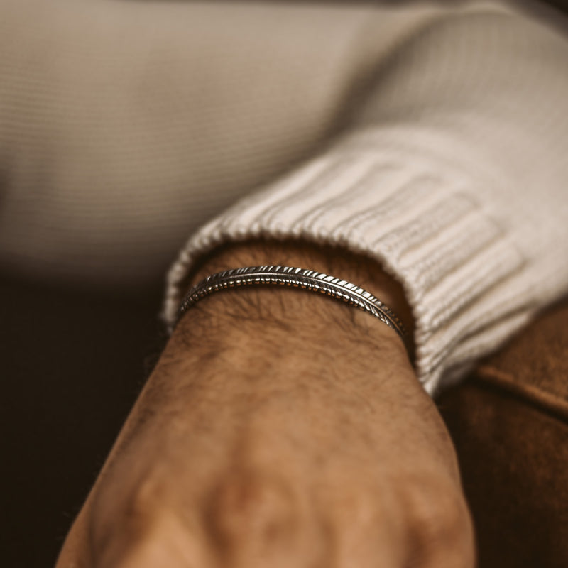 Poignet d'un homme portant le bracelet pour homme « Zahir thin » en argent 925, orné d'une plume, disponible sur Ninetwofive.