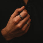 Ein Mann trägt einen schwarzen Pullover und einen Ferran - Oxidierter Sterling Silber Ring 6mm, der eingraviert ist.