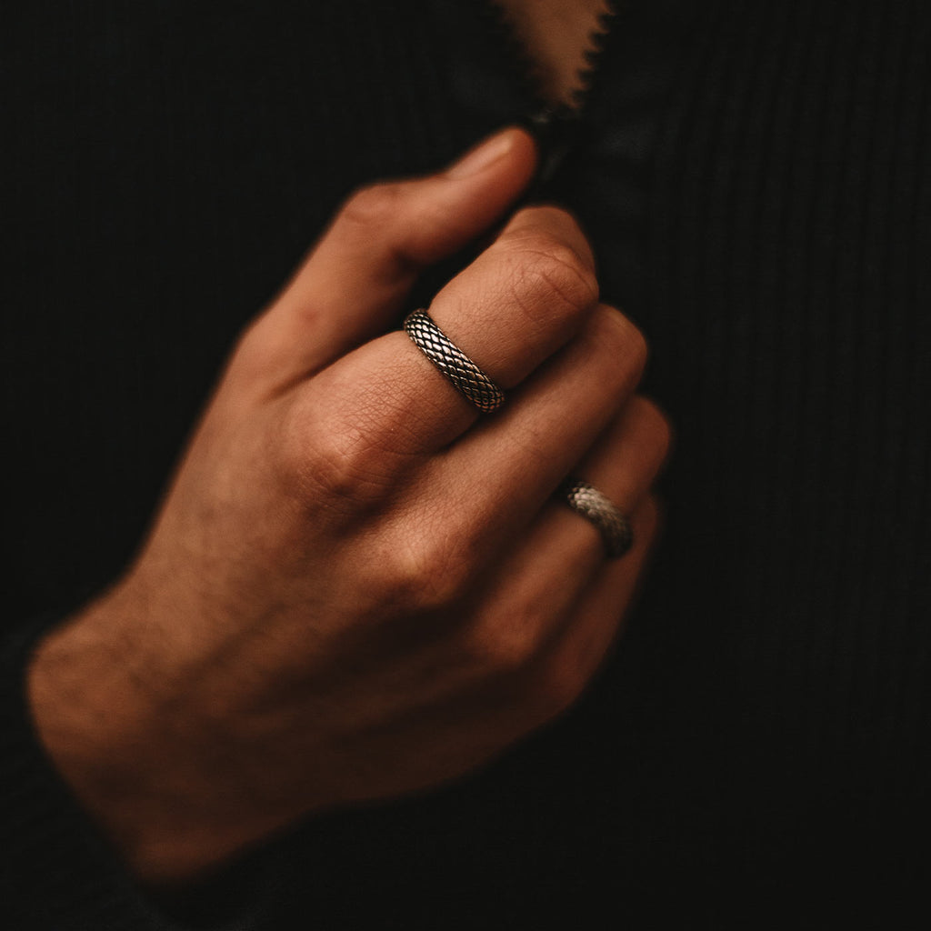 Ein Mann trägt einen schwarzen Pullover und einen Ferran - Oxidierter Sterling Silber Ring 6mm, der eingraviert ist.