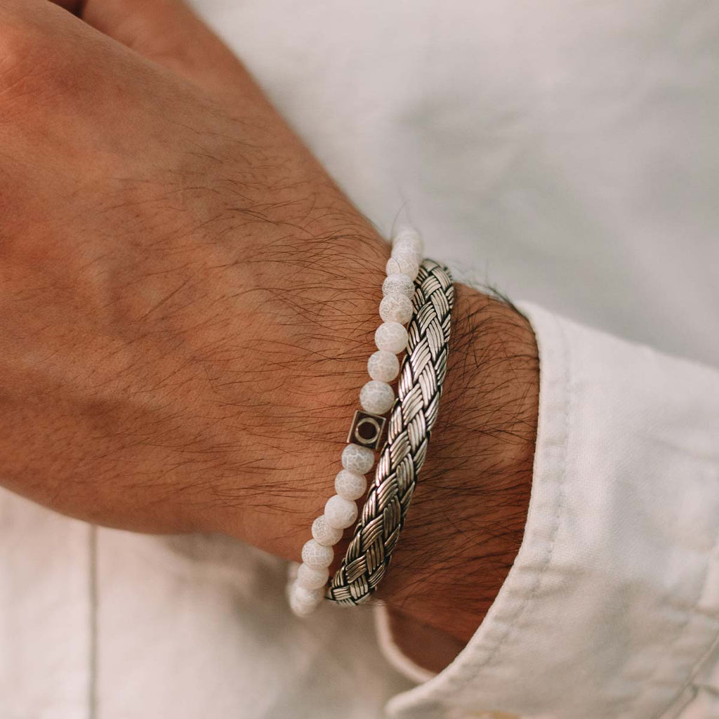 A man wearing the Idris - Braided Silver Bangle Bracelet 8mm with a white stone on it.