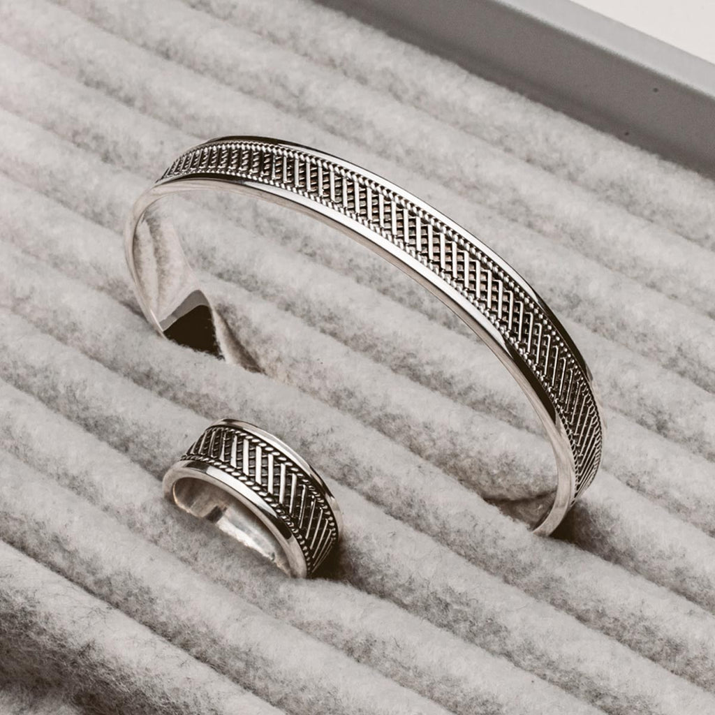 Een zilveren manchetarmband en ring bovenop een box, waarop de Kaliq - Geoxideerde Sterling Zilveren Ring 10mm staat.