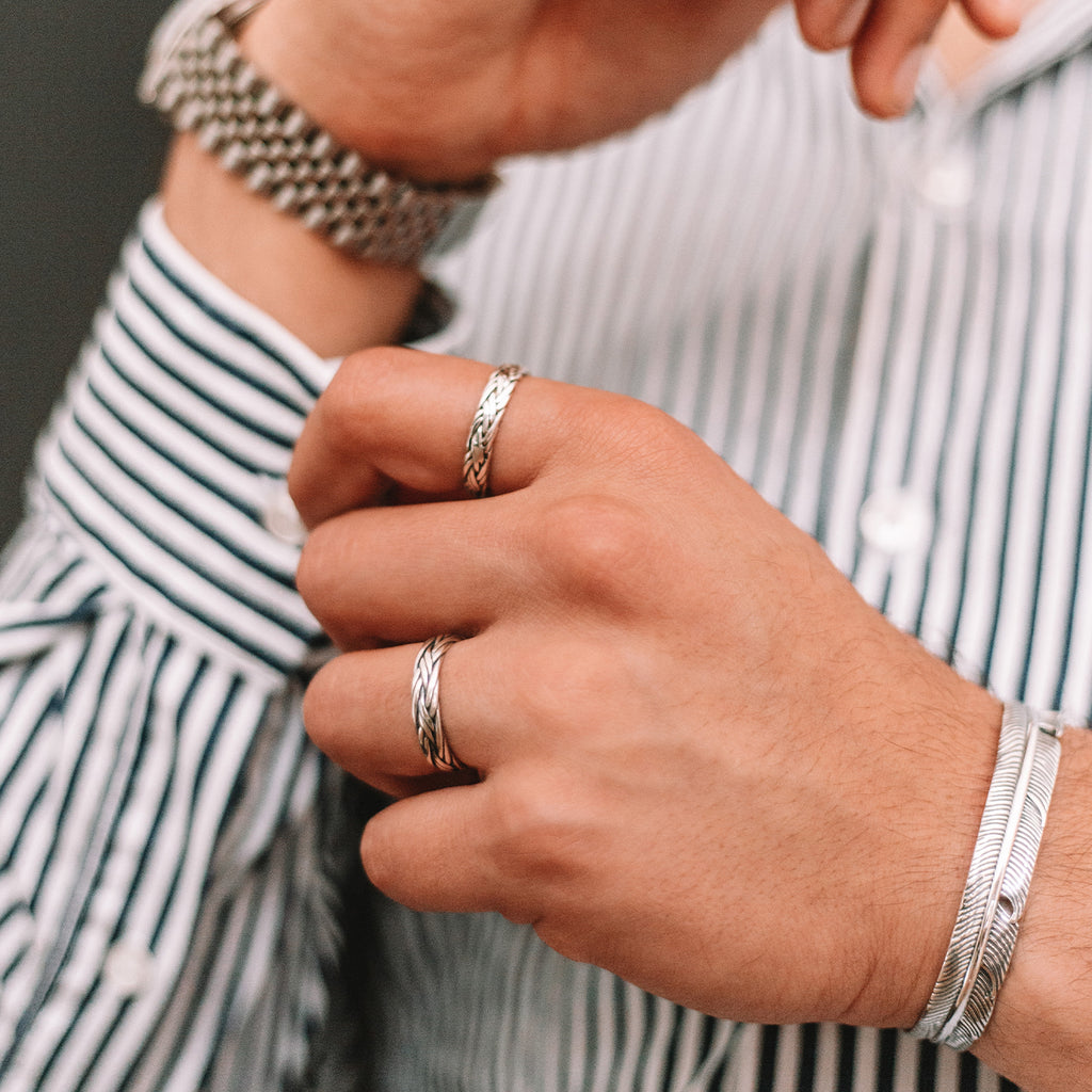 A man wearing a striped shirt and silver rings, including an engraved Latif - Thin Sterling Silver Braided Ring 5mm.