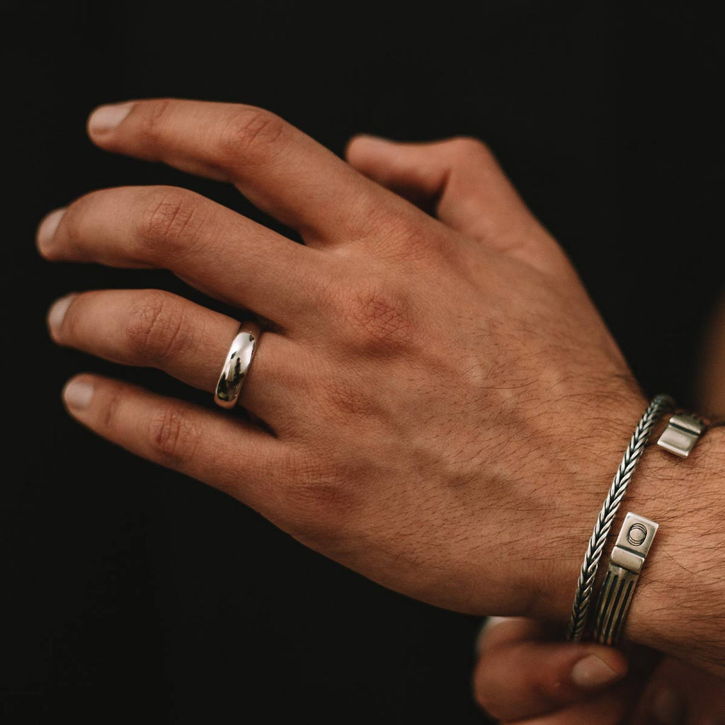 A man's hand adorned with a Malik - Plain Sterling Silver Ring 6mm and bracelet.