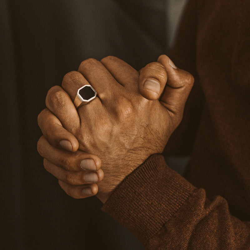 A man in a brown sweater wearing a Naim mens signet ring with an engraved black onyx stone by Ninetwofive. 