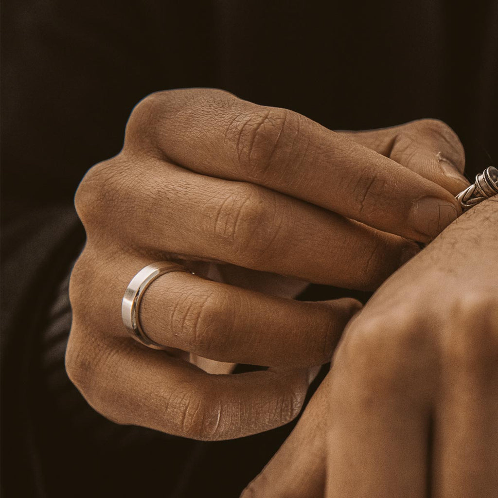 De hand van een man past de Tamir - Matt Silver Ring 6mm om zijn pols aan.