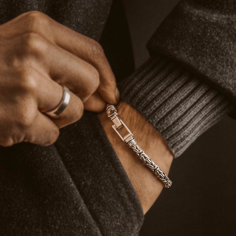 Een man in een zwarte trui houdt de Turath-armband voor heren vast en draagt een ring van sterlingzilver van Ninetwofive.
