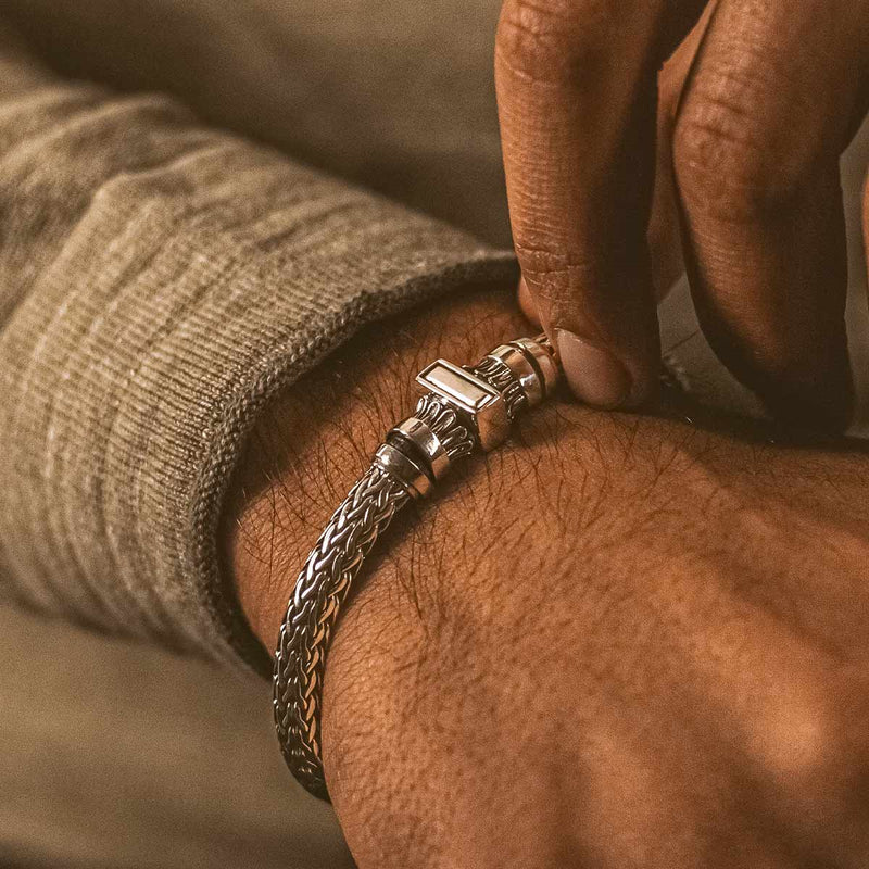 A man in a beige long sleeve shirt is putting on a Mirza 925 silver braided bracelet by Ninetwofive.