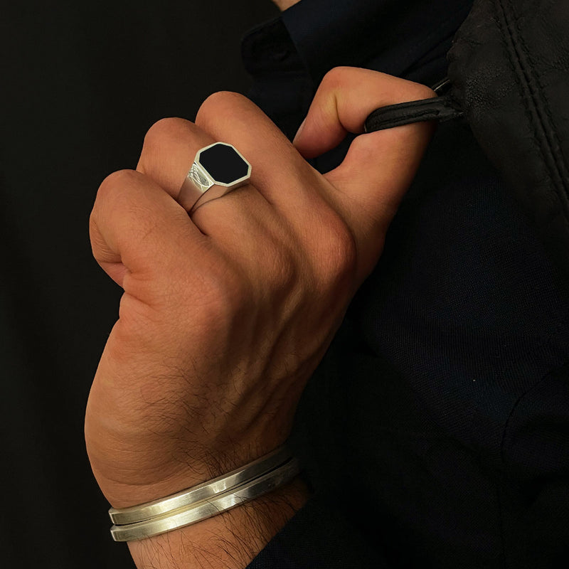 A man in a black long sleeve shirt wearing a Naim black onyx mens signet ring and silver cuff bracelets by Ninetwofive.
