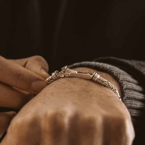 Een man doet de sluiting van een Turath-heren armband van sterlingzilver om zijn pols, Ninetwofive.