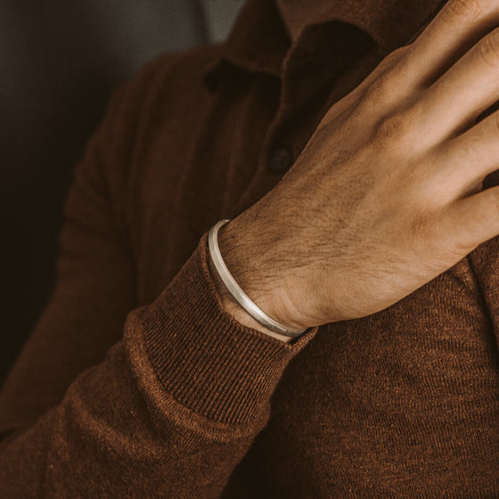 Een man in een bruine trui met lange mouwen en een gepersonaliseerde Noor-Cuff van sterlingzilver voor heren van Ninetwofive.