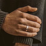 Une main d'homme portant une bague en argent Tamir - Matt de 6 mm, mettant en valeur une bague en argent gravée pour homme.