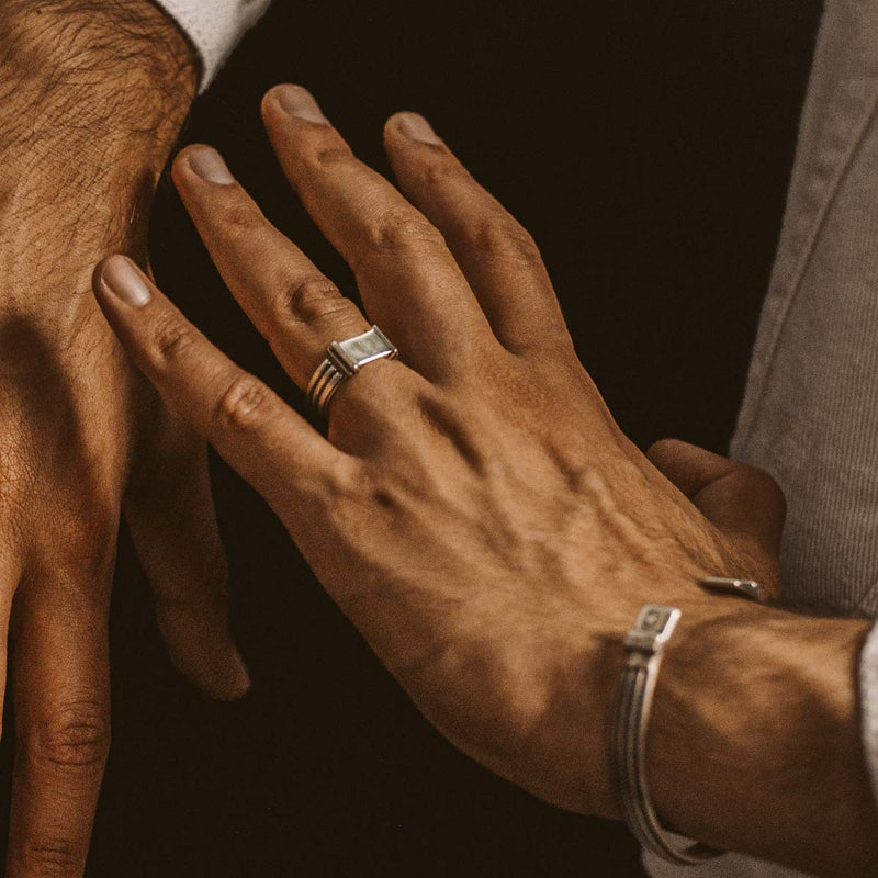 Die Hand eines Mannes, an der ein Imad-Siegelring aus Sterlingsilber und ein Herrenarmband zu sehen sind.
