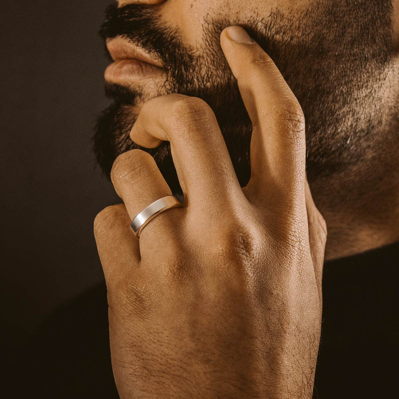 Ein Mann mit Bart trägt den gravierten Herrenring „Tamir“ in mattem Silber von Ninetwofive am Ringfinger.