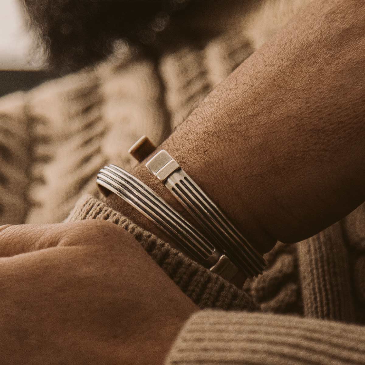 Ein Mann trägt einen Pullover und ein Paar Manschettenarmbänder, darunter das Arkan - Sterling Silver Armreif 8mm.