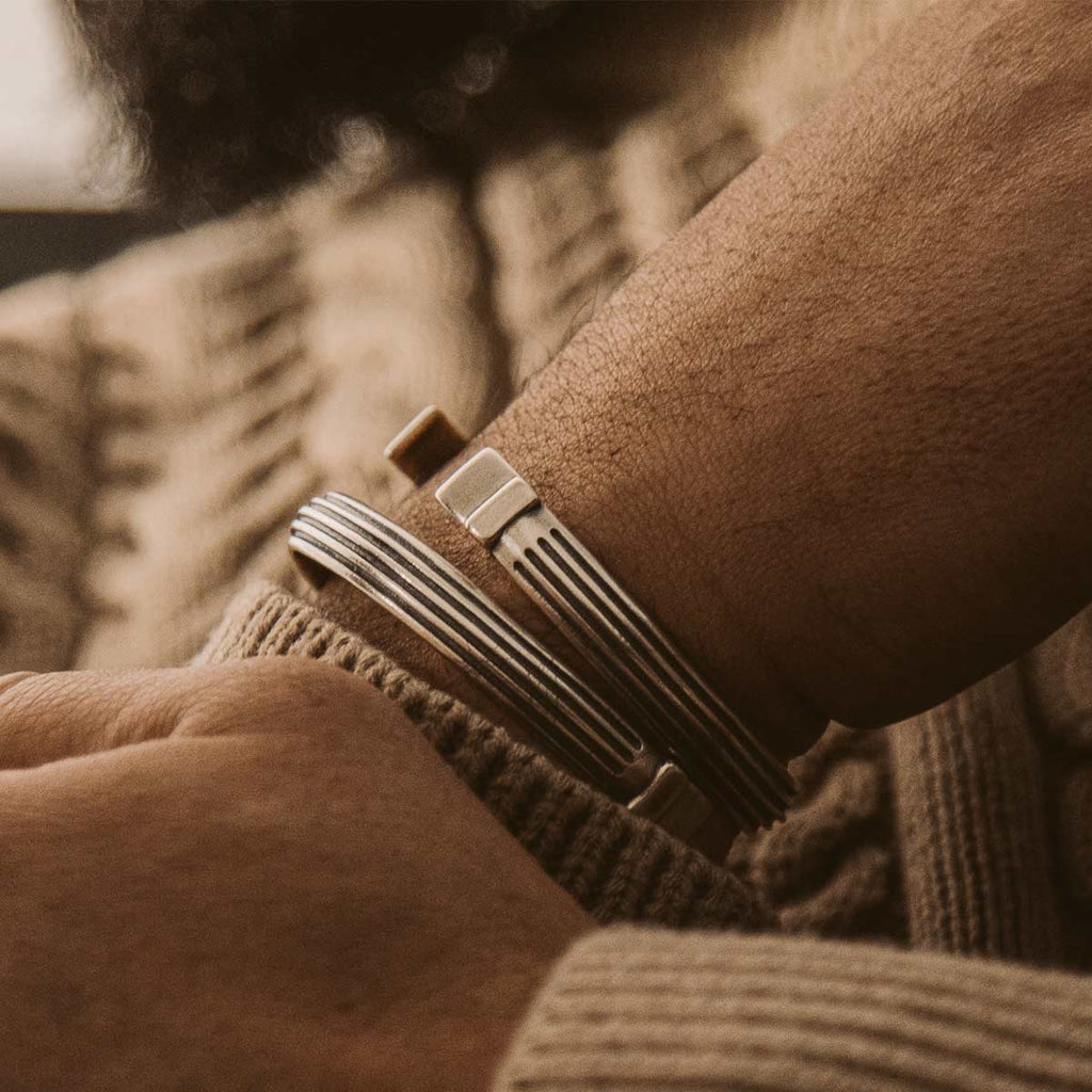 A man wearing a sweater and a pair of cuff bracelets, including the Arkan - Sterling Silver Bangle Bracelet 8mm.