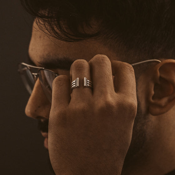 Ein Mann mit Brille, der den Armreif „Mateen“ aus oxidiertem Sterlingsilber für Herren von Ninetwofive in der Hand hält.