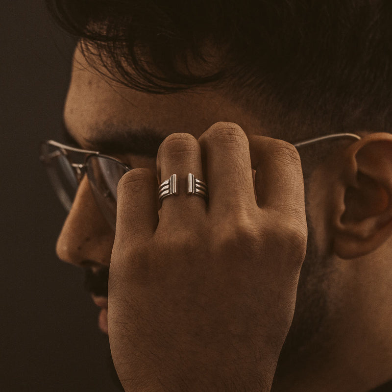 Ein Mann mit Brille, der den Armreif „Mateen“ aus oxidiertem Sterlingsilber für Herren von Ninetwofive in der Hand hält.