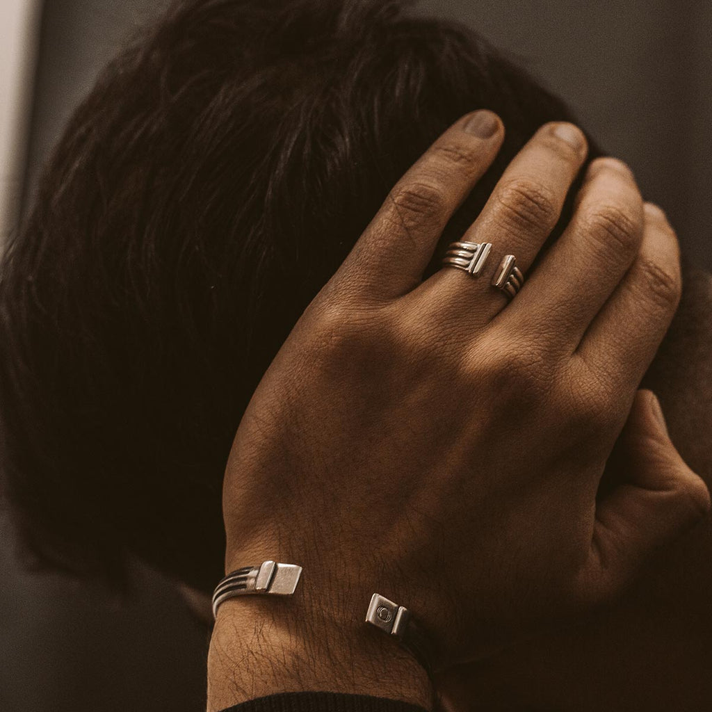 A man wearing the Mateen - Oxidized Sterling Silver Bangle Ring 10mm pair of silver cuff bracelets with an engraved mens ring.