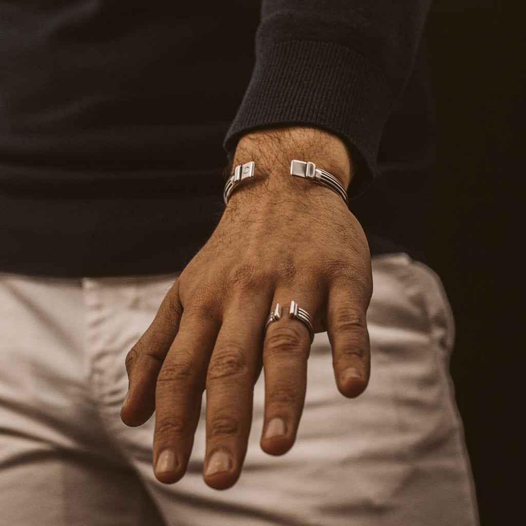 A man wearing a set of Arkan and Mateen - handmade, oxidized silver cuff bracelets.