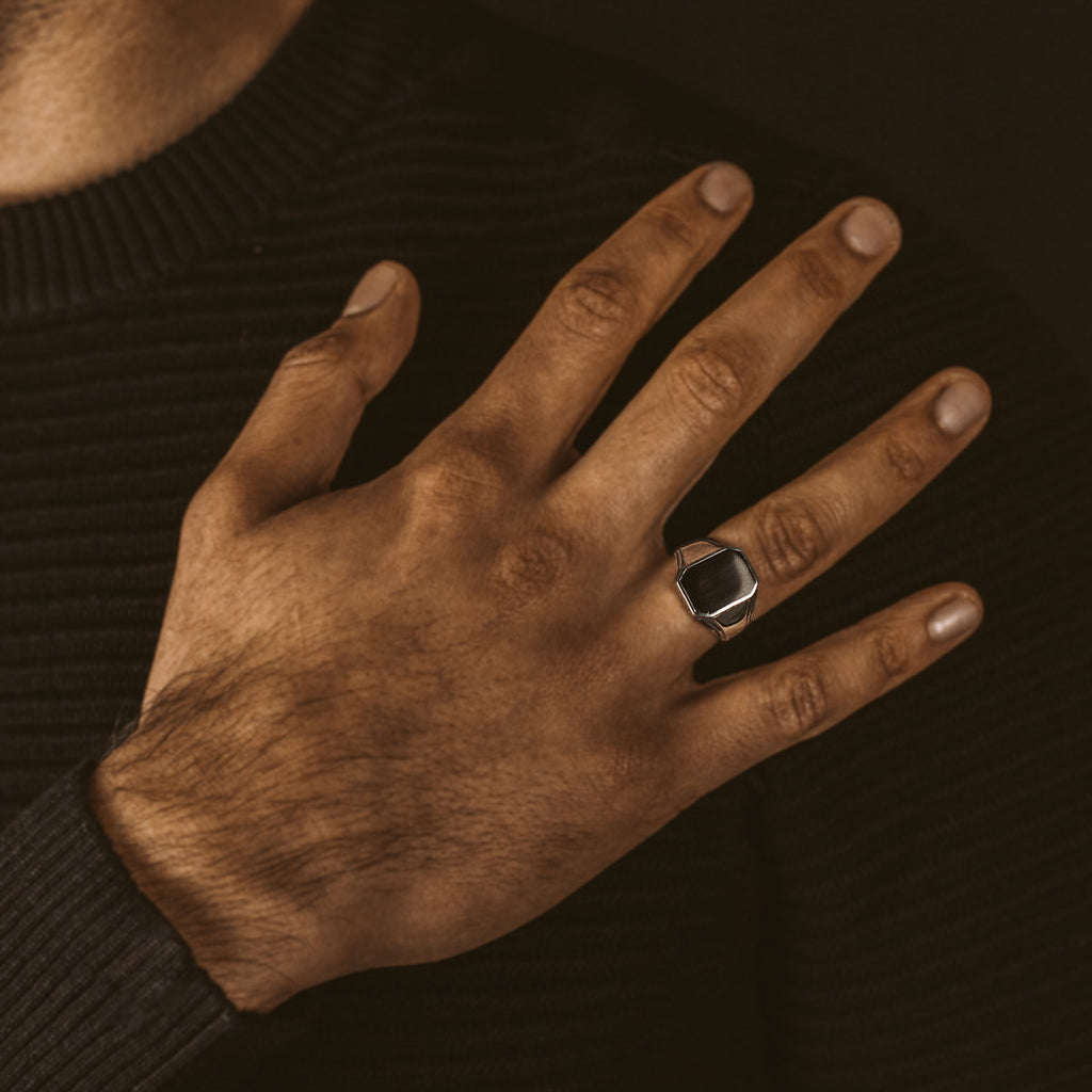 Een man draagt een NineTwoFive zwarte trui met een Baki - Black Onyx Zegel Ring 17mm aan zijn hand, met een onyx zegel.