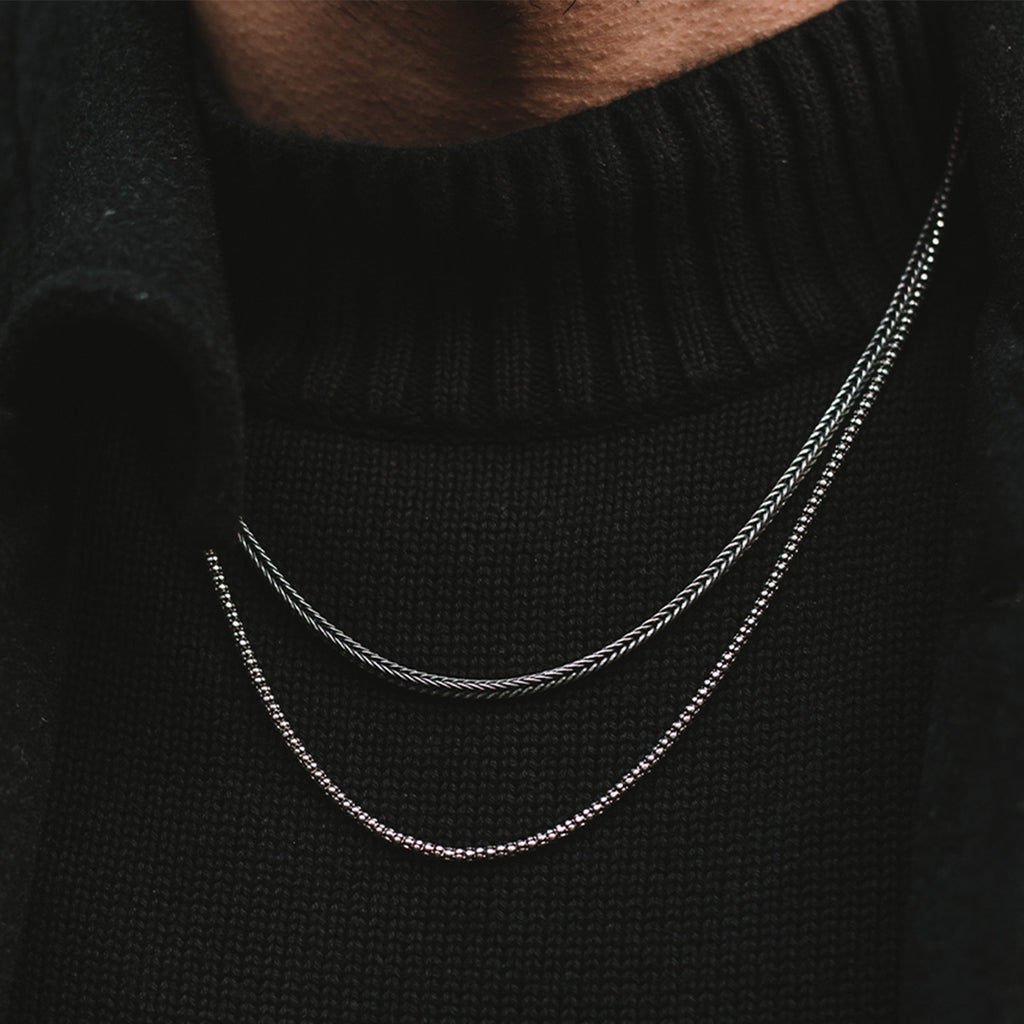 A man wearing a black sweater and an Anis - Sterling Silver Wheat Chain Necklace 3mm.