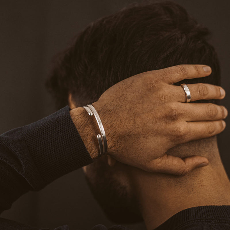 Een man in een zwarte trui die de Noor-manchetarmband van sterlingzilver en de Tamir-zilveren set van Ninetwofive draagt.