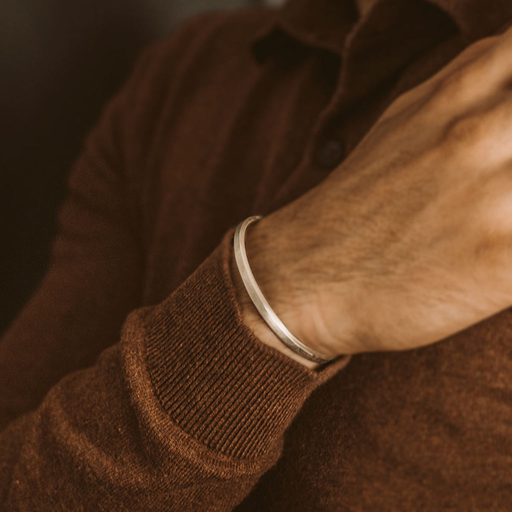 A man wearing a brown sweater and a silver Boulos and Noor - set cuff bracelet that is handmade.