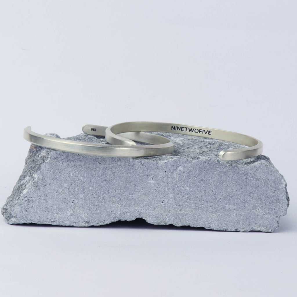 Twee Noor - Geborsteld Zilver Bangle Armbanden 5mm bovenop een rots.