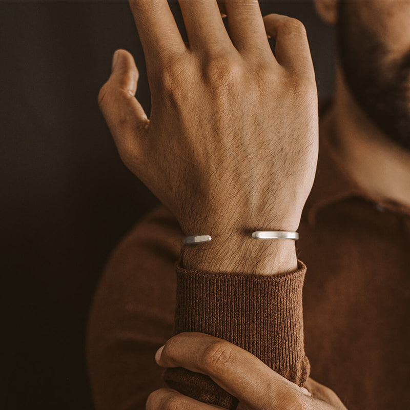 Een man in een bruine trui die de sterling zilveren cuff-armband voor heren van Ninetwofive draagt.