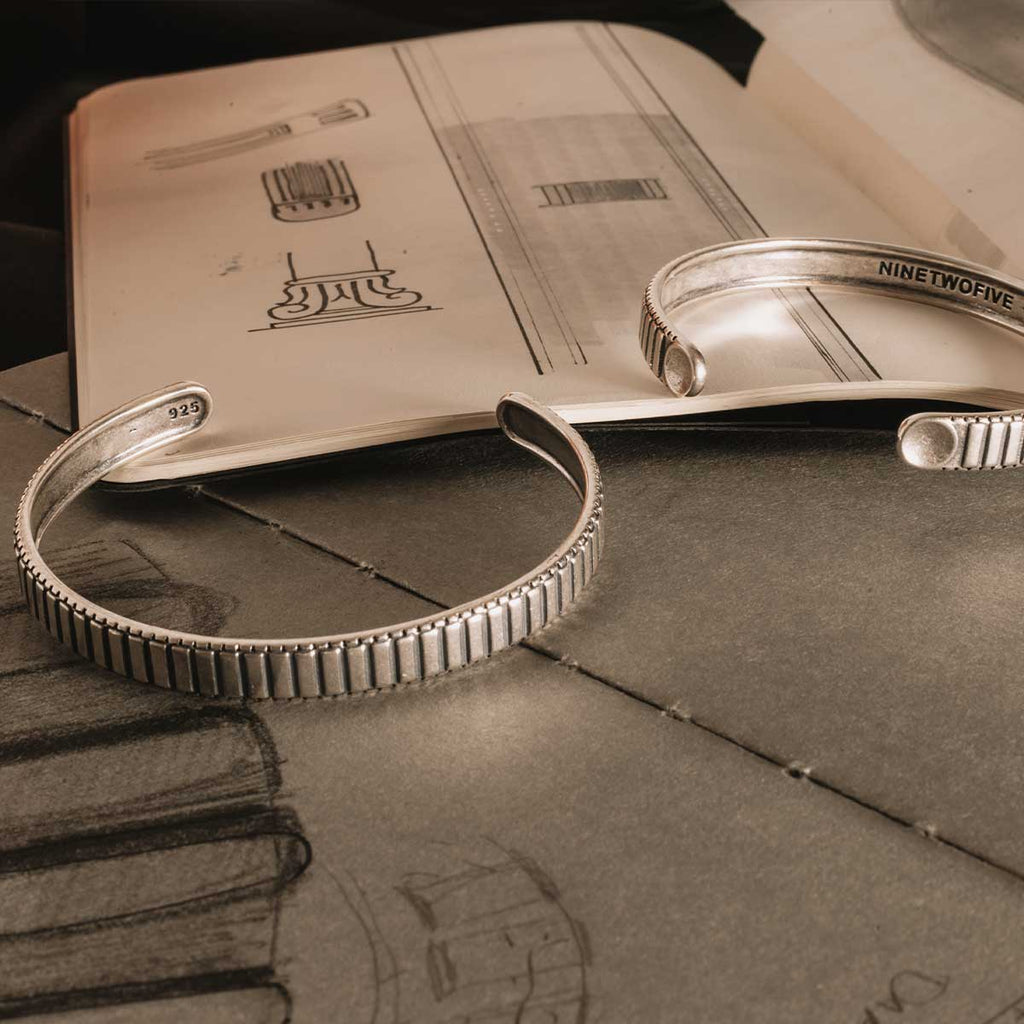 Une paire de bracelets Kenan - Jonc en argent sterling, posés sur un livre, parfaits pour les hommes qui apprécient les accessoires personnalisés.