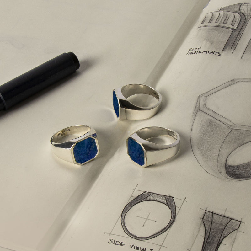 Three Kadar blue stone mens signet ring designs on a piece of sketch paper and black pen.