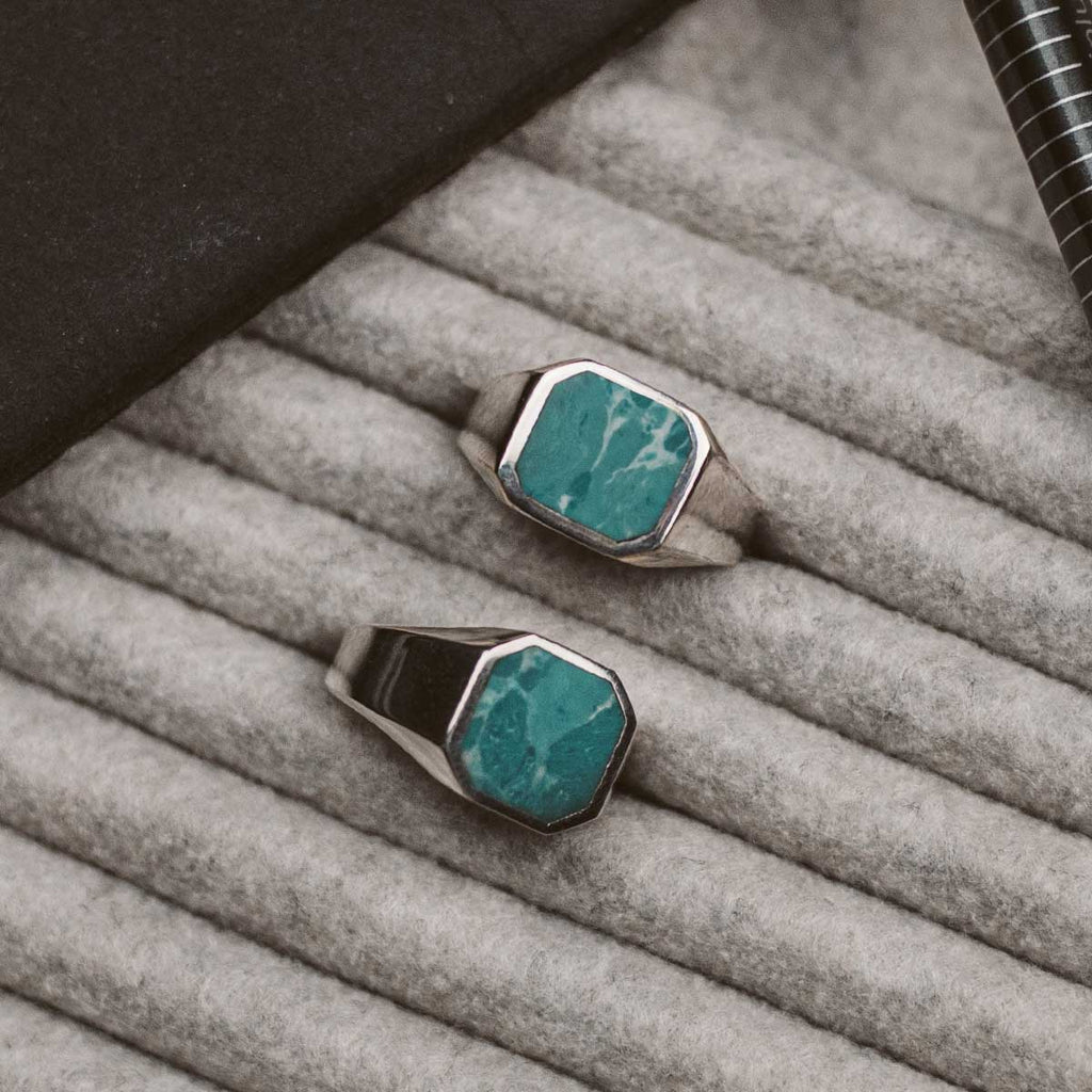 Two Nuri - Sterling Silver Blue Turquoise Signet Rings, one engraved, sitting on a table.