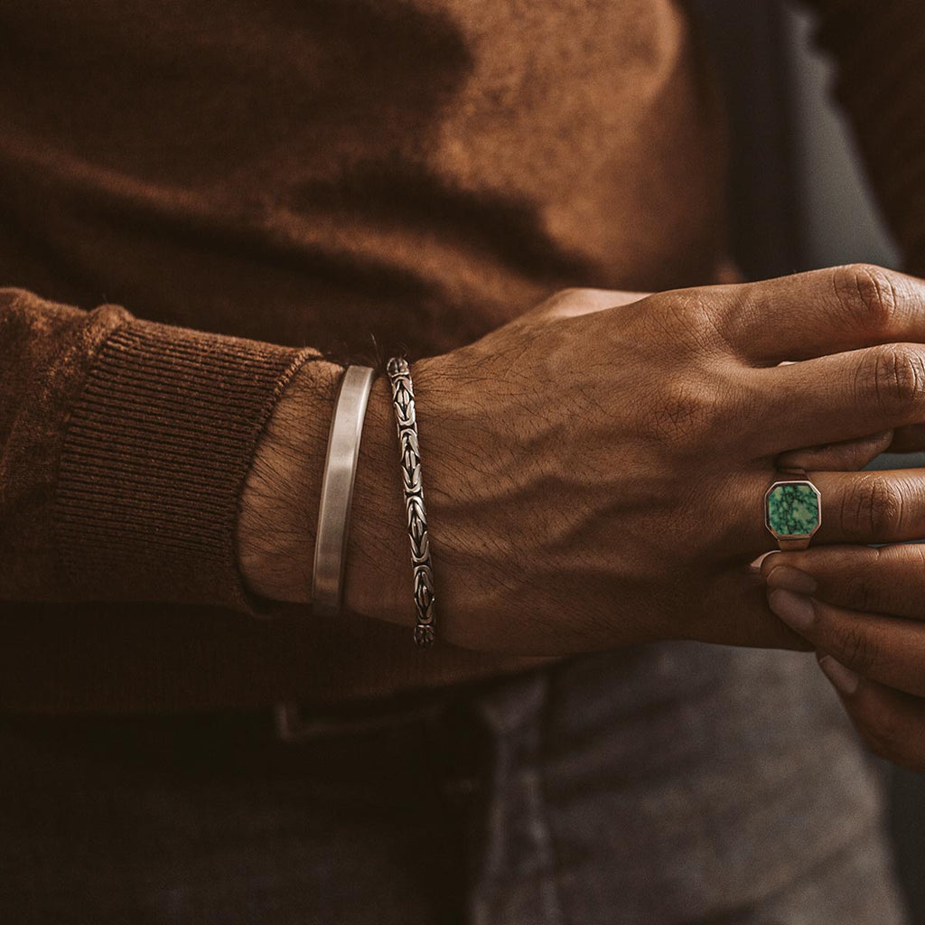 A man wearing a Boulos - Plain Sterling Silver Bangle Bracelet 8mm with an emerald stone.