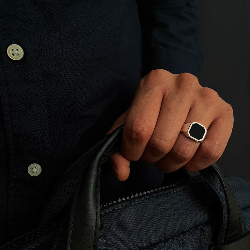 A man button black shirt holding an Naim black onyx mens signet ring in a blue bag.
