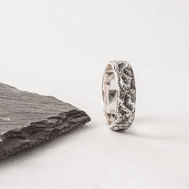 A Tarif sterling silver mens ring engraved for him, placed on a piece of slate.