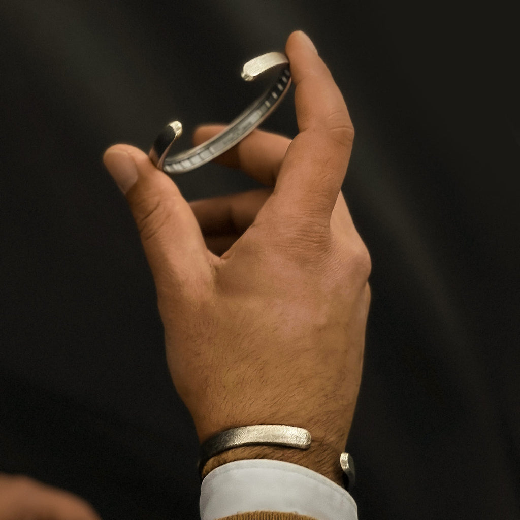 Die Hand eines Mannes hält einen Fudail - Rough Brushed Sterling Silver Bangle 8mm, ein massives Silberarmband für Männer.