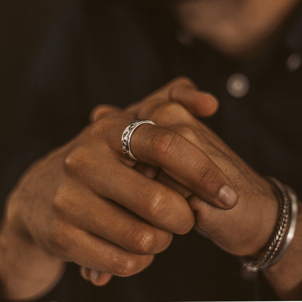 Een man draagt een Tarif - Unieke Sterling Zilveren Ring 7mm met een gravure op zijn hand.
