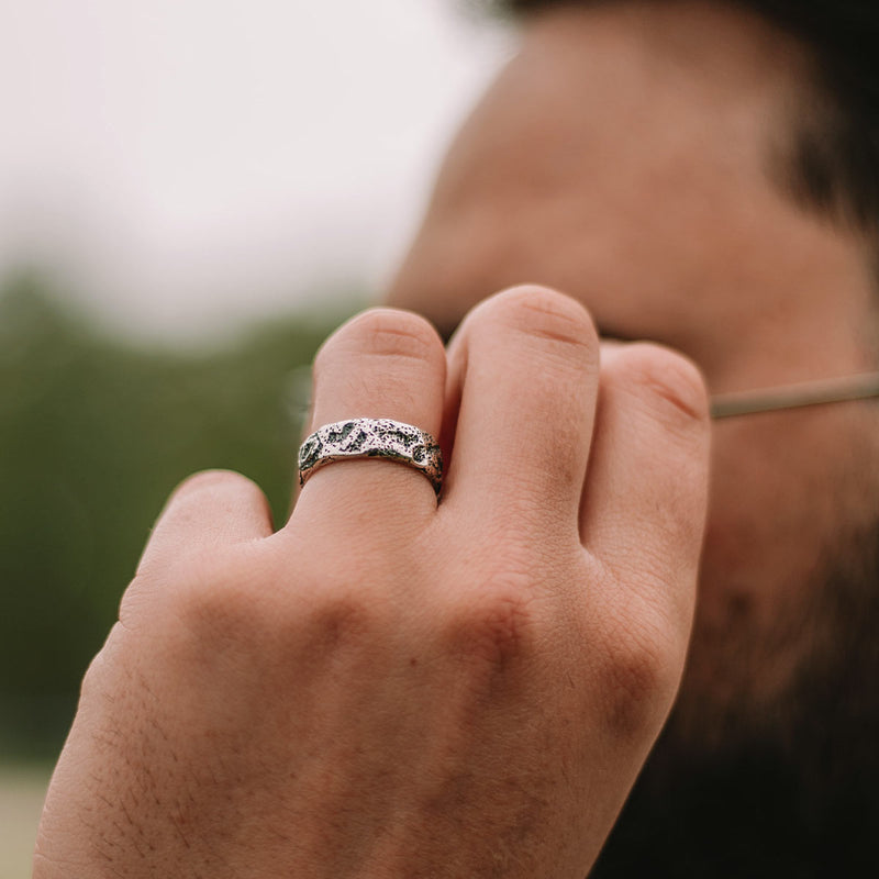 A man with a beard is holding the glasses while wearing Tarif sterling silver mens ring on his ring finger.