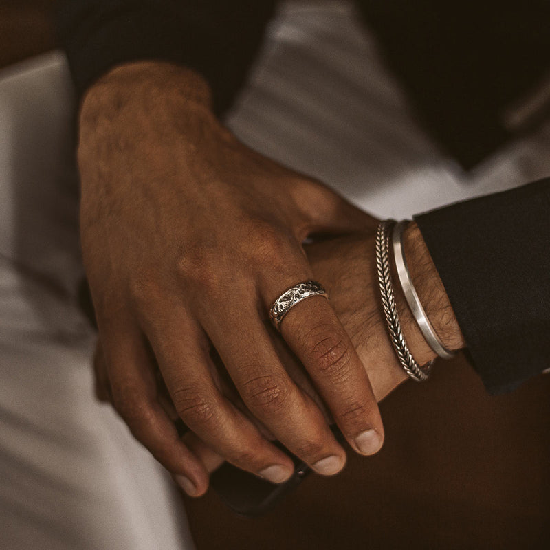 Man wearing a black long sleeve shirt and white pants, displaying the Tarif sterling silver mens ring and Ninetwofive bracelets.