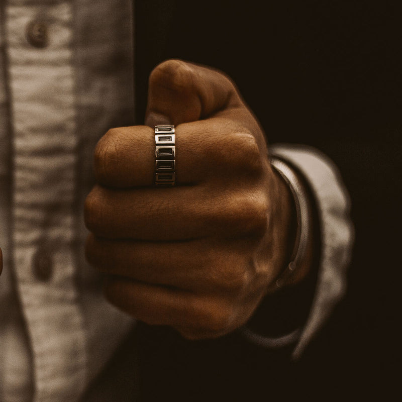 Een man in pak houdt een Yardan geoxideerde sterling zilveren heren ring van Ninetwofive vast.