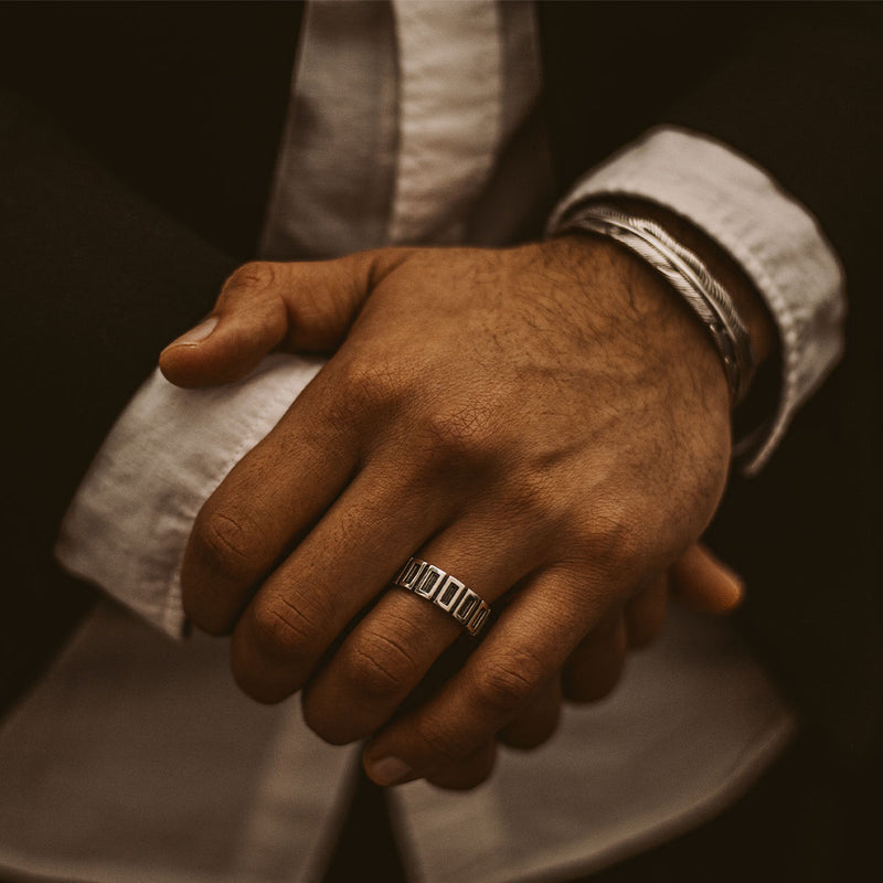 Een close-up van de handen van een man die een Yardan geoxideerde sterling zilveren heren ring van Ninetwofive vasthoudt.