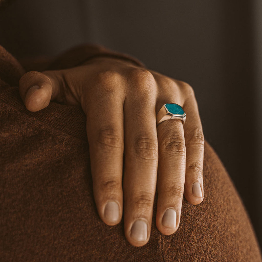 Eine Frau trägt einen Nuri - Sterling Silver Blue Turquoise Signet Ring 13mm mit einem gravierten turquoise Stein.