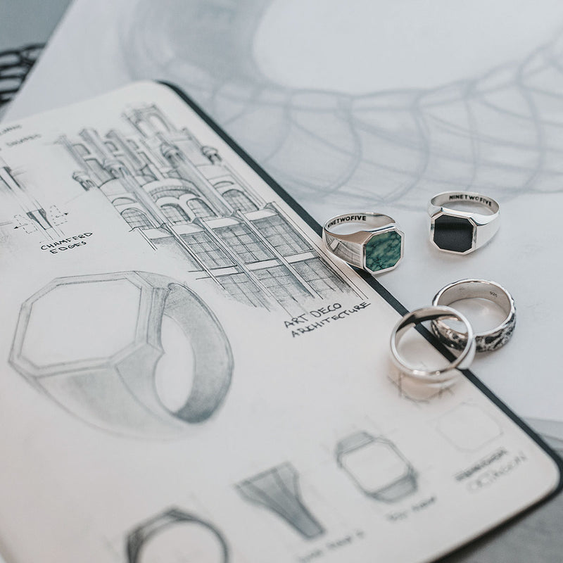 A sketch of a Naim black onyx mens signet ring and silver rings on top of a notebook from Ninetwofive