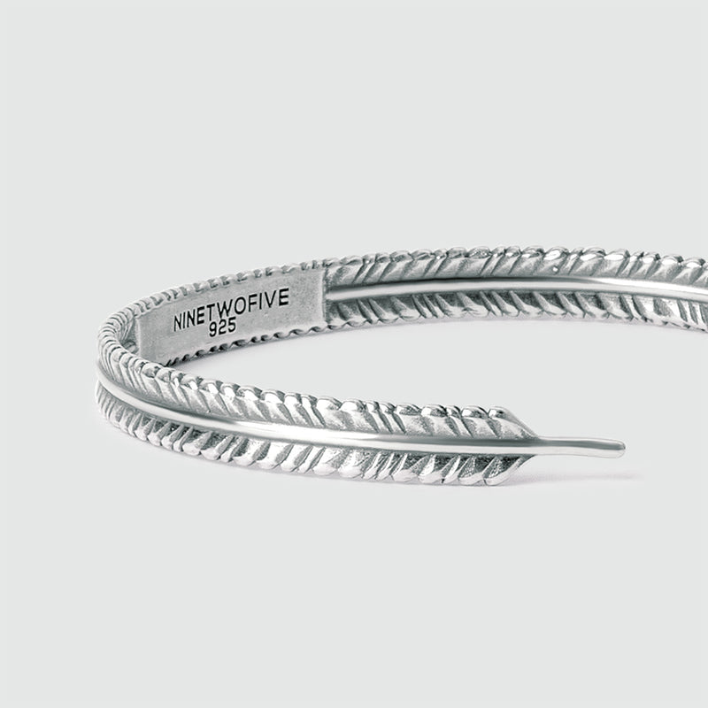 Vue en angle du bracelet pour homme « Zahir » massif, en argent avec motif de plume, montrant l'espace intérieur prévu pour une gravure gratuite par Ninetwofive.