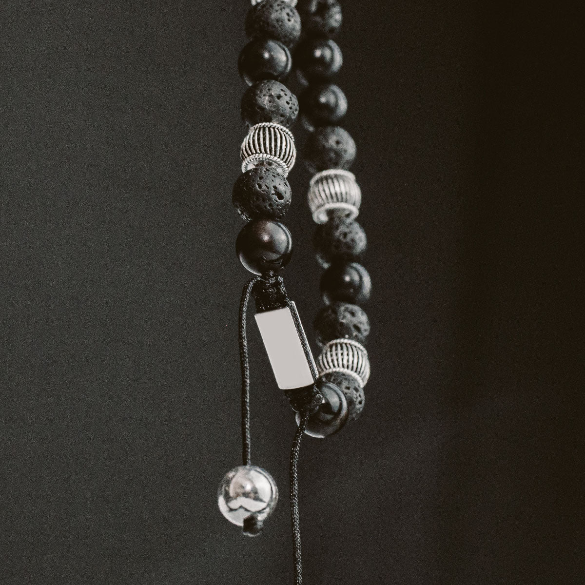 A black and silver beaded bracelet hanging on a background.
